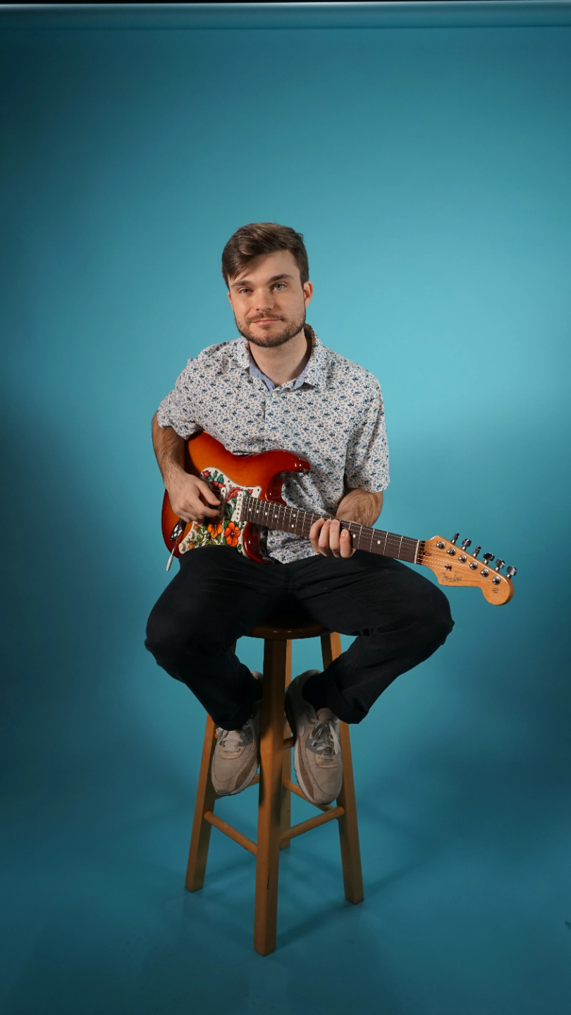 Luke Broadbent, a Maestro Music guitar and uke teacher, sitting on a stool holding an electric guitar