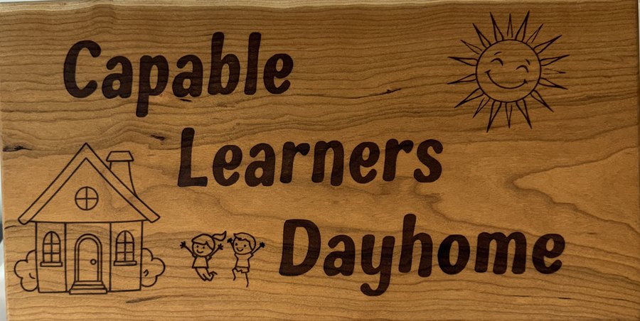 Kayla's wooden sign: Capable Learners Dayhome, with a little house, a smiling sun and two jumping kids