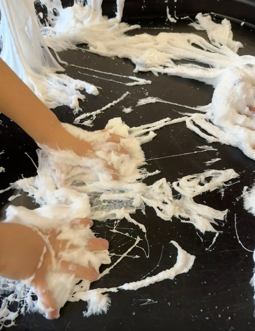 Child's hands pulling and squishing white spiderweb slime during sensory play