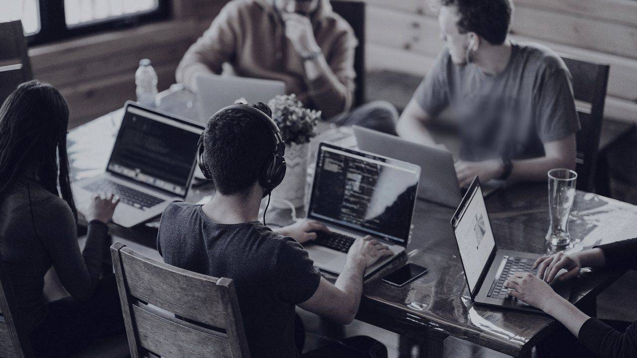Equipo de trabajo colaborando con laptops en una mesa de oficina con luz natural.