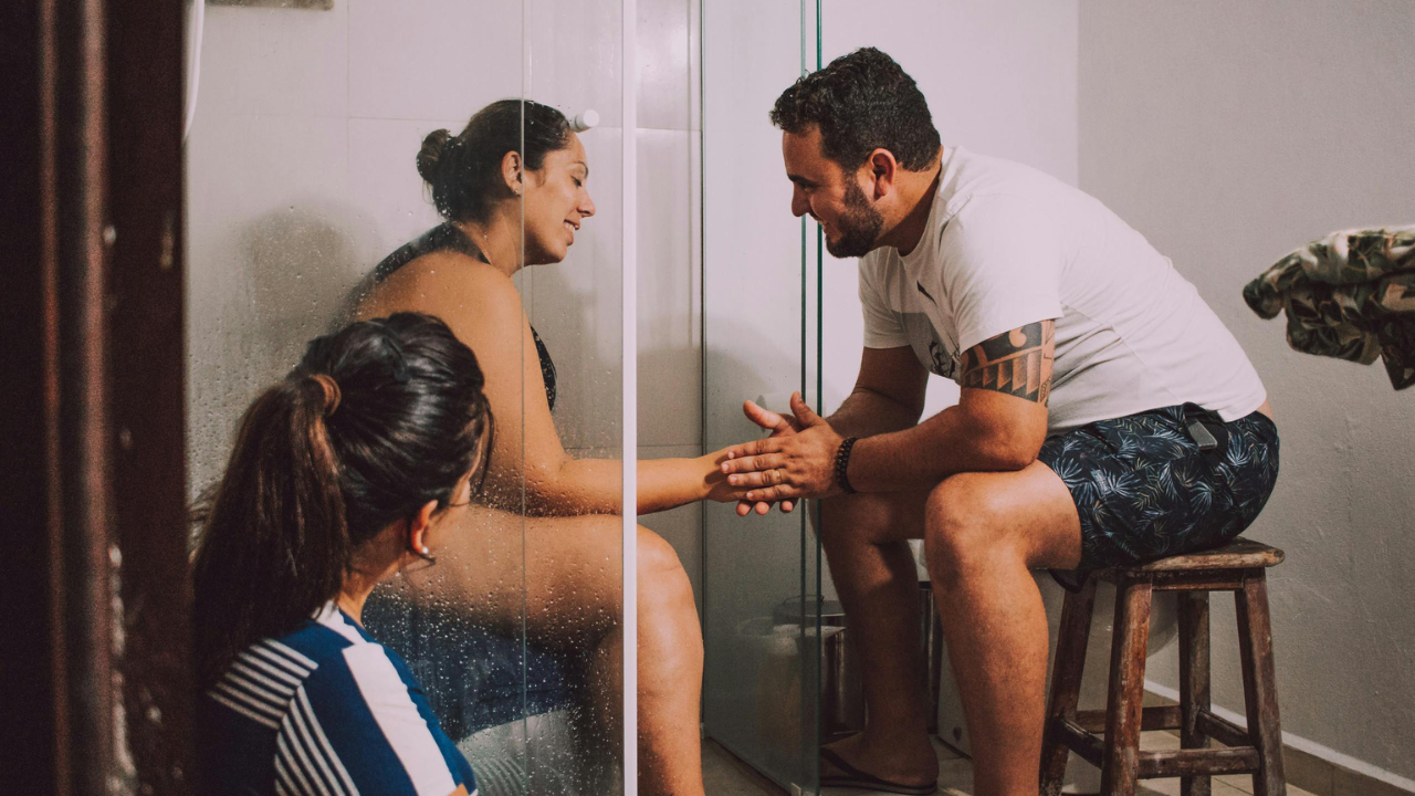 A doula watching a laboring person in the shower while their partner holds their hands