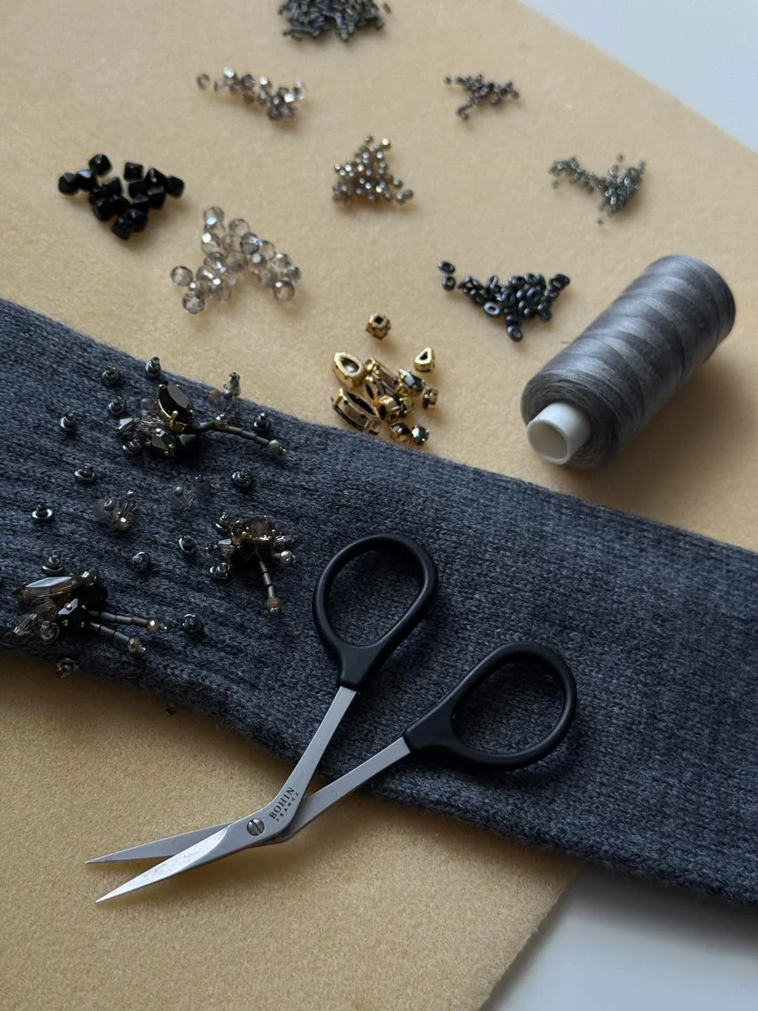 Grey sock being hand-embroidered with beads and crystals, scissors and thread