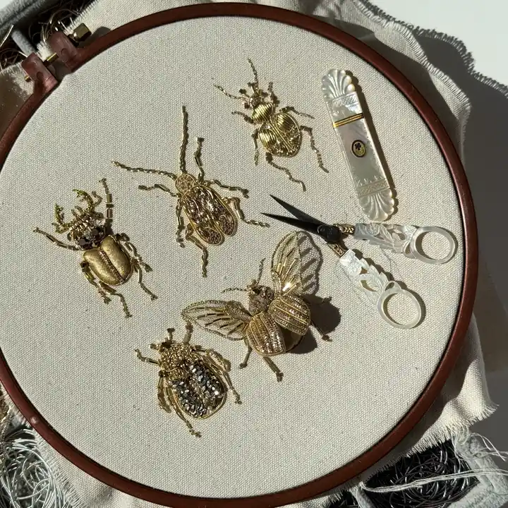 Top-down view of goldwork beetle brooches with mother-of-pearl embroidery tools
