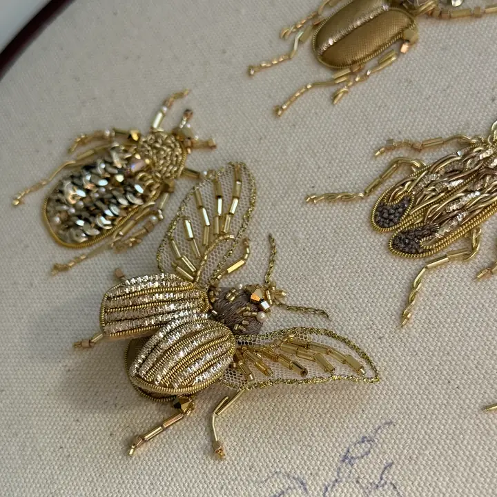 Close-up of golden beetle brooches in metal-thread goldwork embroidery