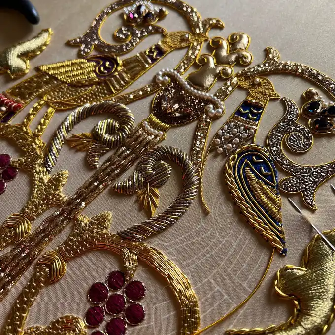Close-up of goldwork embroidery with red jewels, pearls and gold purl scrollwork
