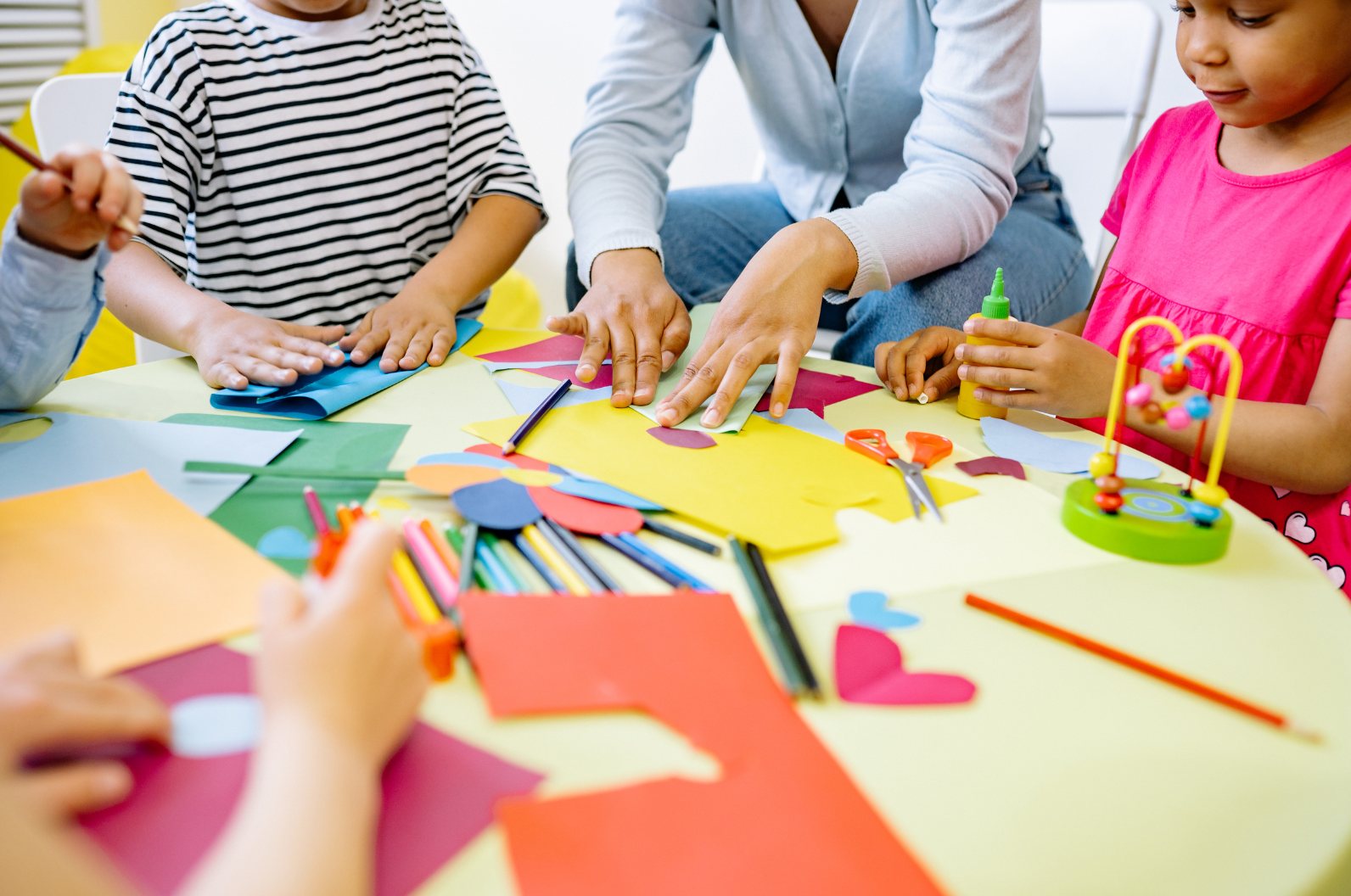 Children cutting and gluing coloured paper with an educator