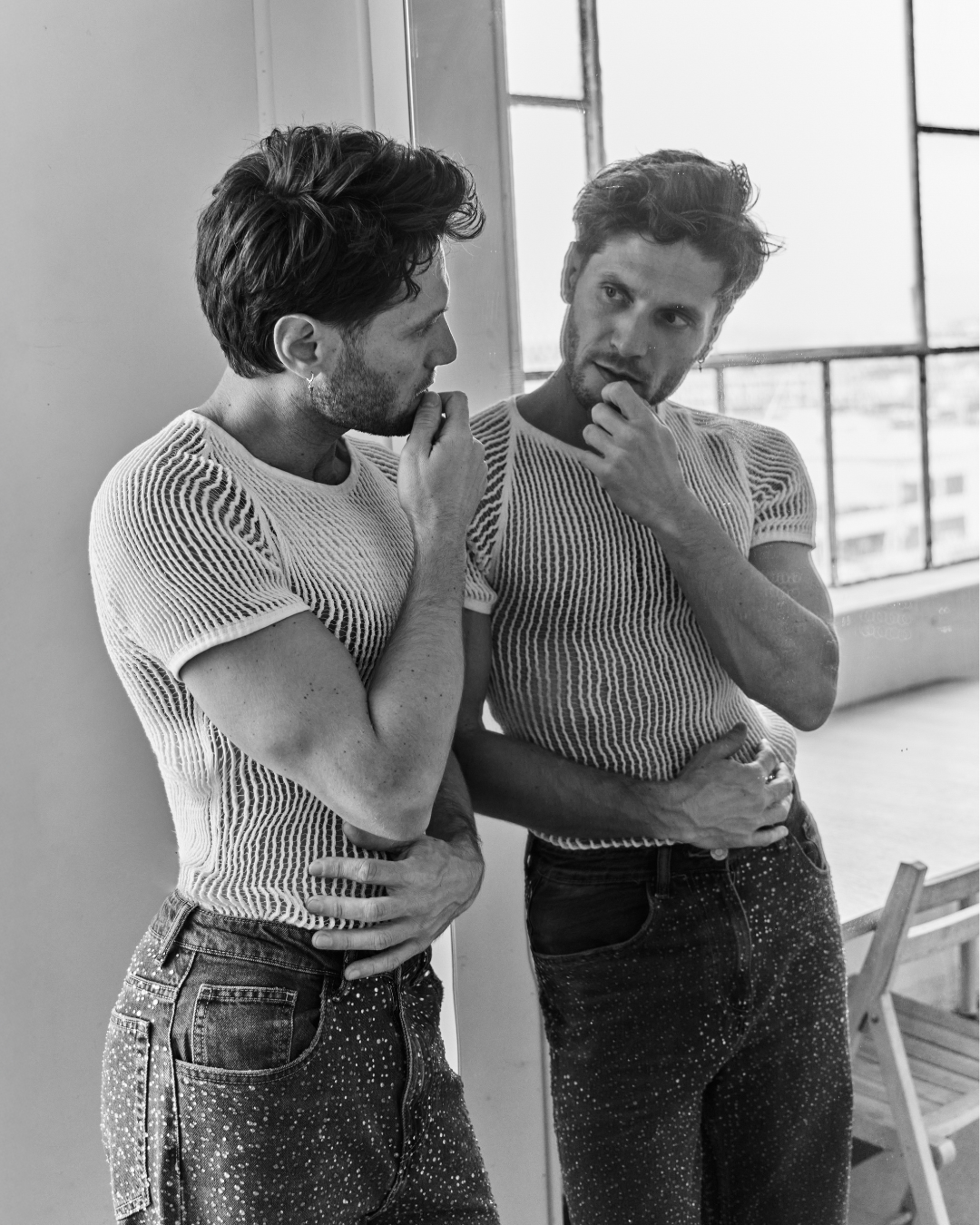 Alessandro and his reflection, hand at his mouth, in a mesh shirt