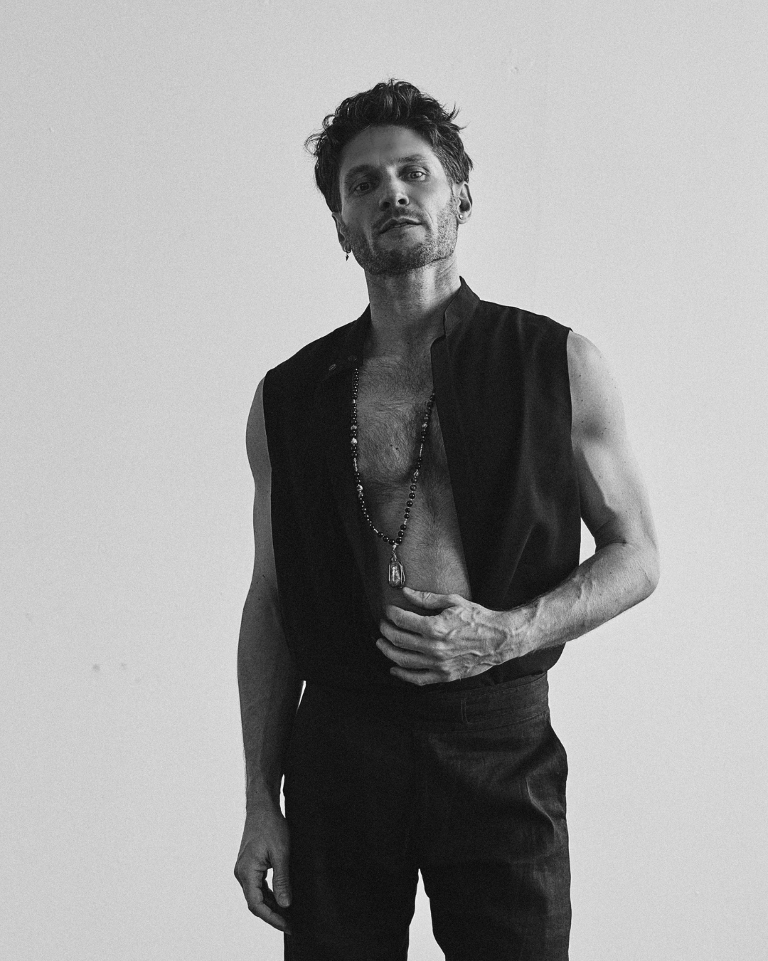Alessandro in an open black vest, looking straight into the camera