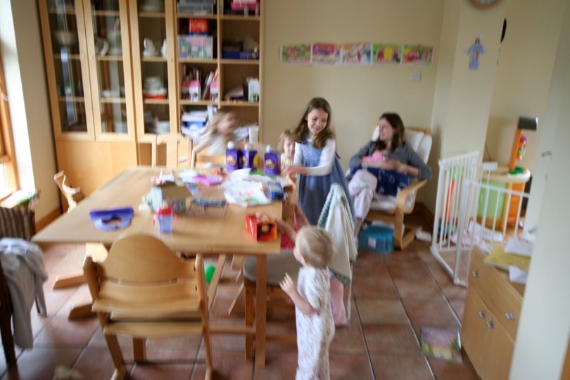 Kate feeding baby in the kitchen, children around her