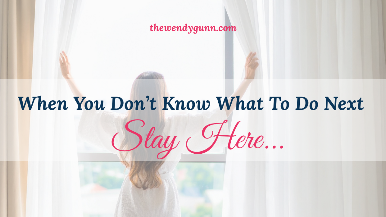 “When You Don’t Know What To Do Next Stay Here" blog graphic featuring a woman standing by a bright window opening white curtains, symbolizing seeking God’s guidance, trust, and taking the next step with faith from The Wendy Gunn.