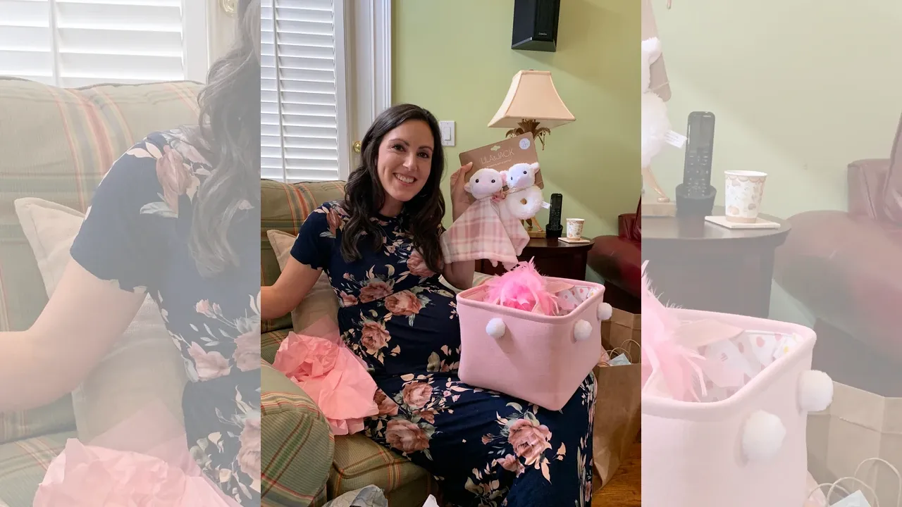 Pregnant woman at 37 weeks sits in a chair at her baby shower, holding up pink baby items and smiling. 