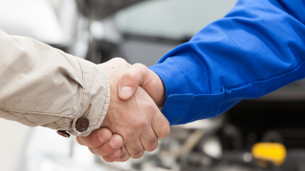 Two people shaking hands beside a vehicle