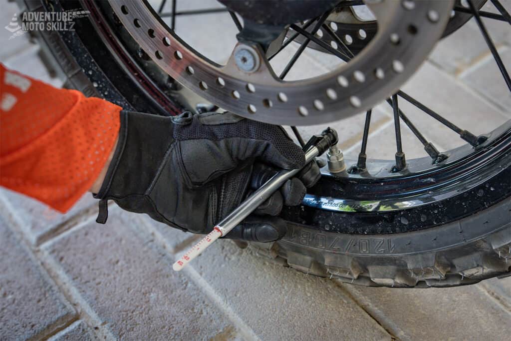 Checking motorcycle tire pressure with a pencil tire pressure gauge