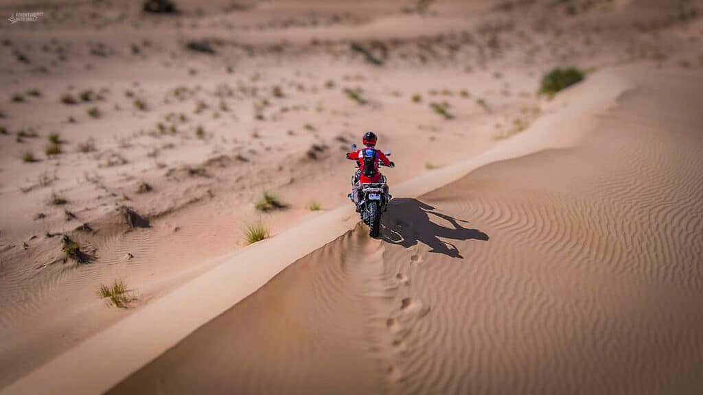 Motorcycle and rider on top of a sand dune in the desert