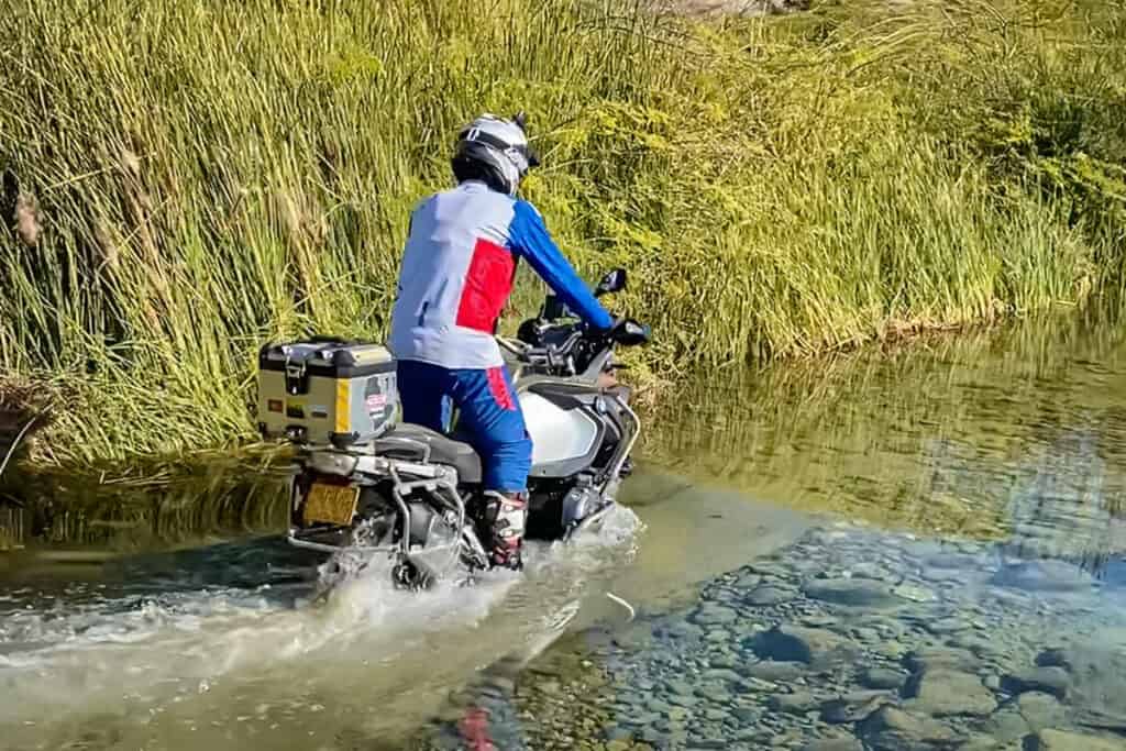 ADV motorcycle rider standing on the pegs during a water crossing