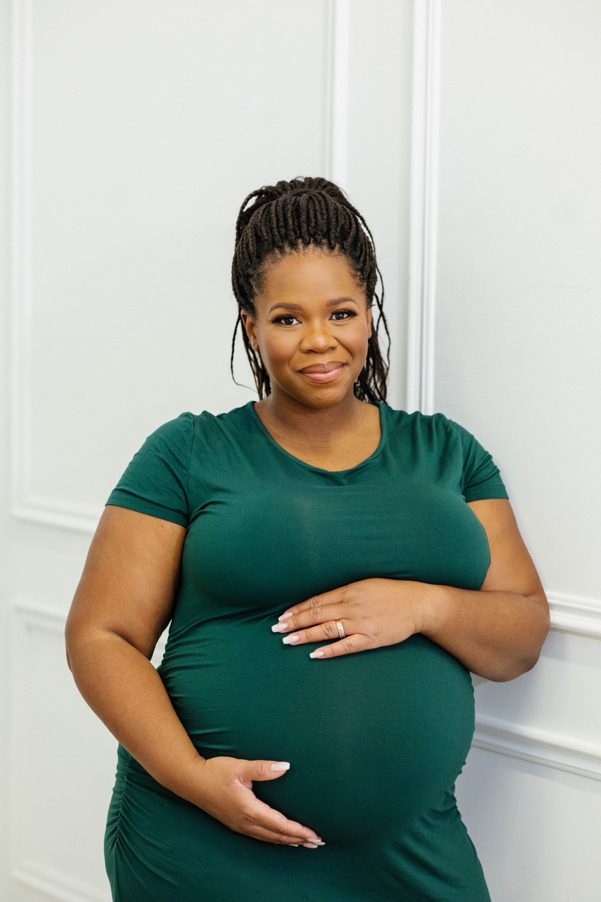 Sophie in a green dress, smiling, with a hand on her pregnant belly