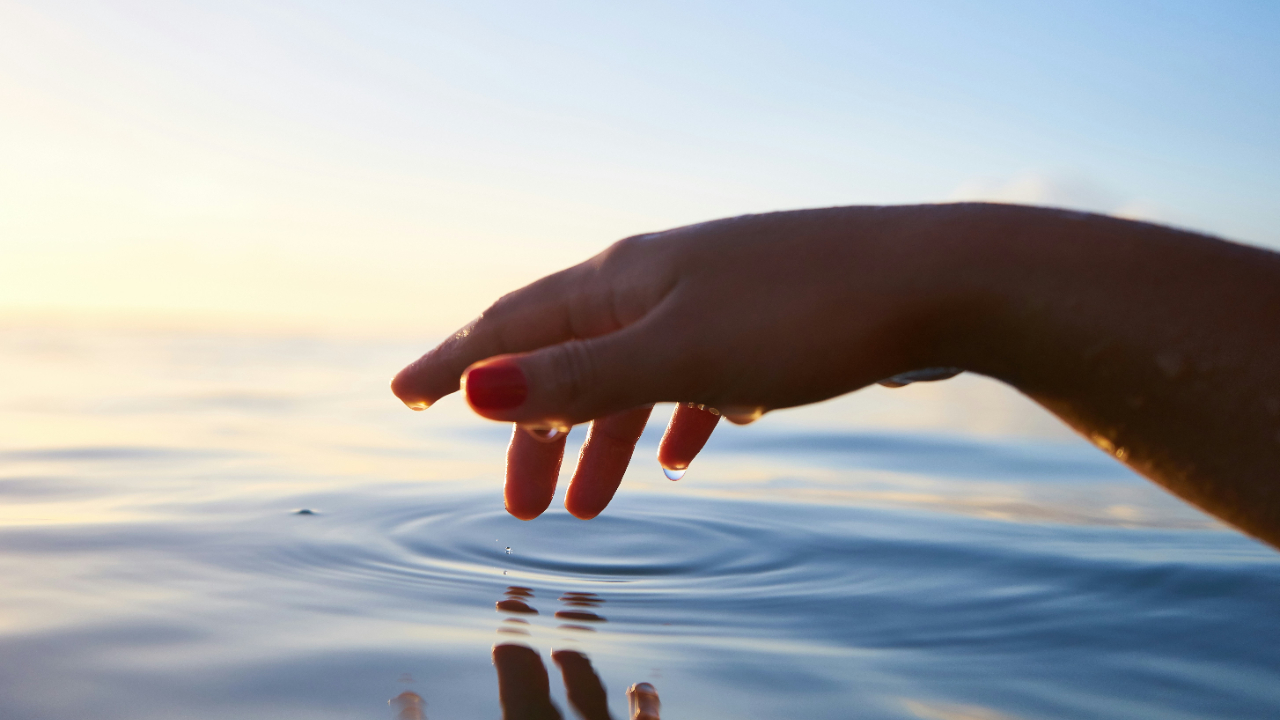 Hand gently tapping water to make ripples.