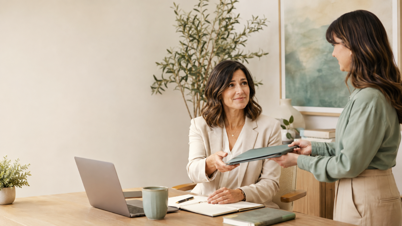 A professional woman accepts another folder from a colleague with a polite but hesitant expression, reflecting people-pleasing and difficulty setting boundaries.
