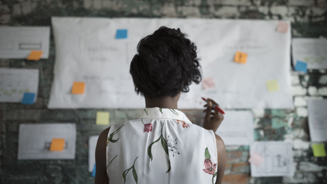 Woman reviewing ideas and notes on a wall, representing adaptive thinking and navigating change.