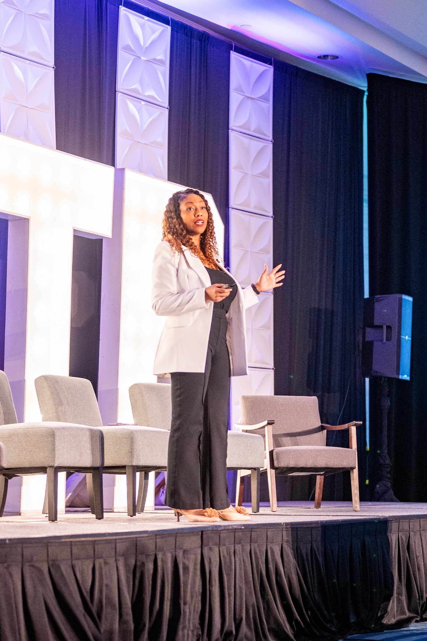 Dr. Rachel Gainsbrugh delivering a live keynote in a white blazer