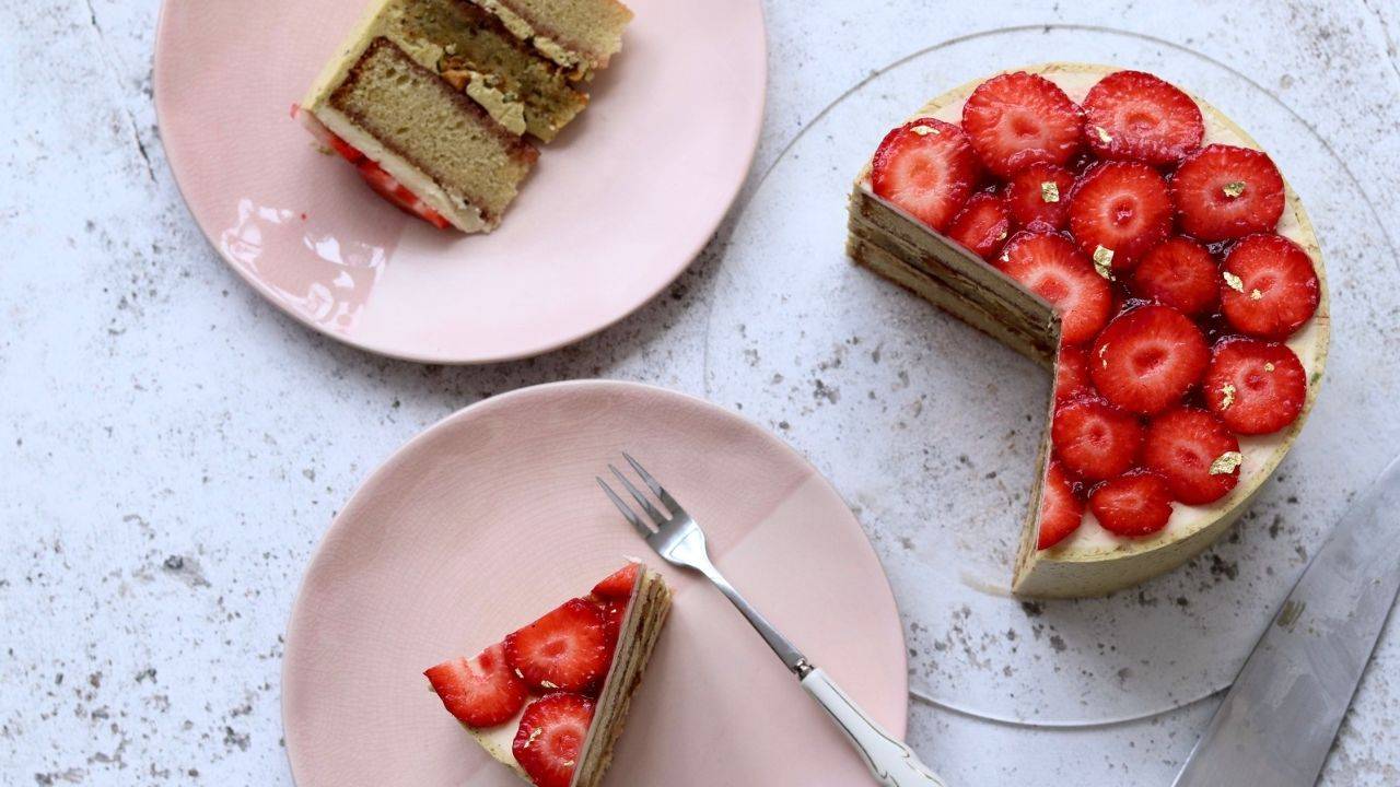 Layered strawberry cake with gold leaf, sliced to show the cream layers