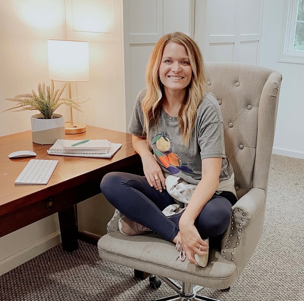 Jess smiling in a tufted chair beside her desk