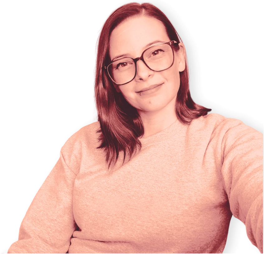 Britt, smiling in glasses and a coral sweatshirt, leaning into the camera