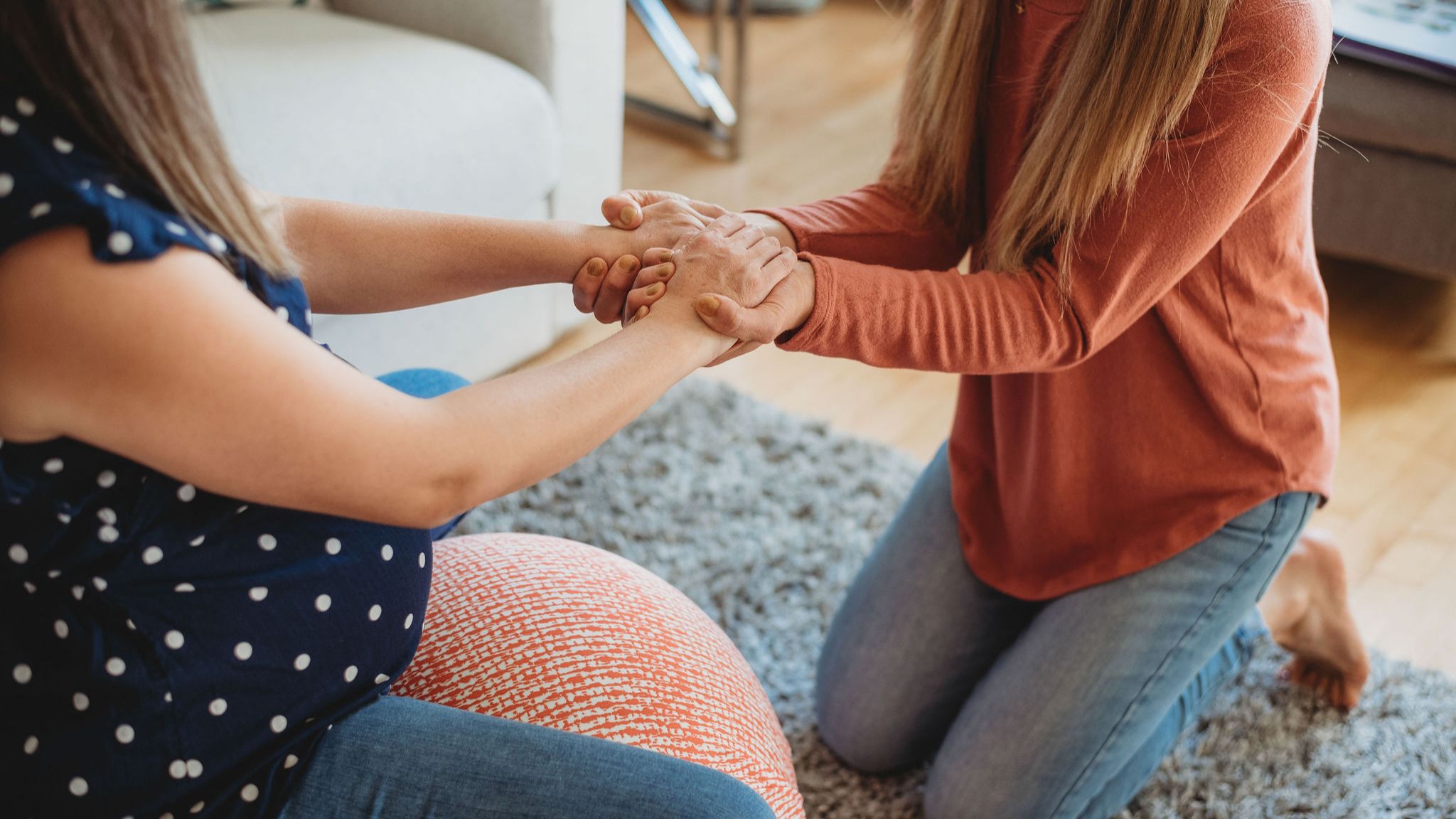 Pregnant woman sitting on ball while holding hands with the woman sitting in front of her