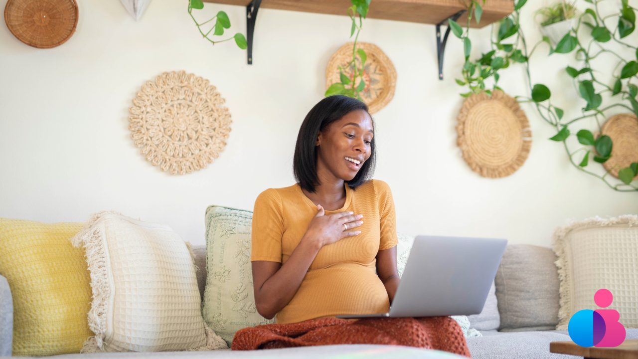 Pregnant woman sitting on a couch speaking to a laptop
