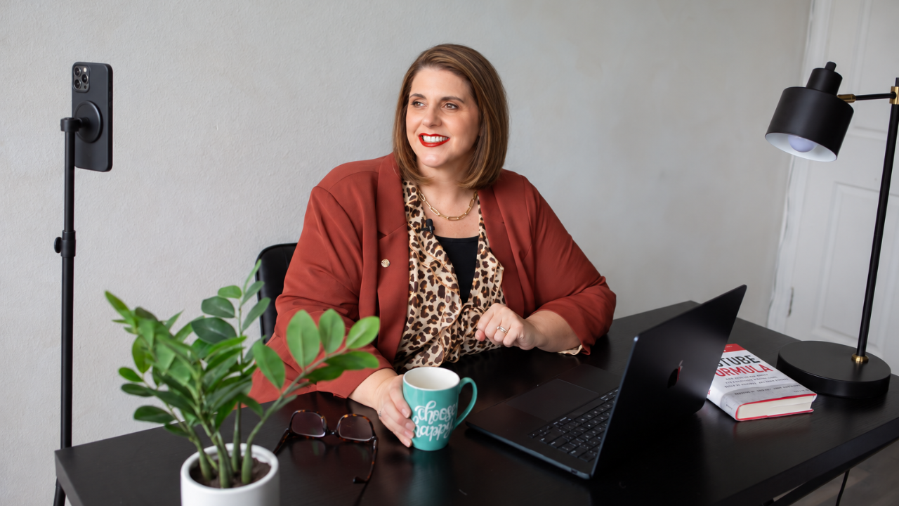 Kathy Sizemore at her desk filming on a phone mounted on a tripod, a simple YouTube studio setup at home.