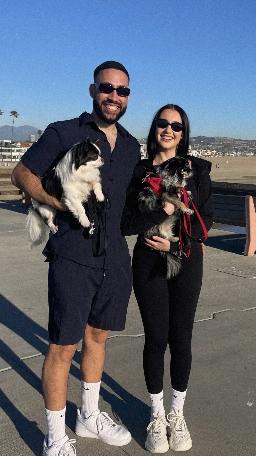 Kyra and her partner holding their two chihuahuas on a beach pier