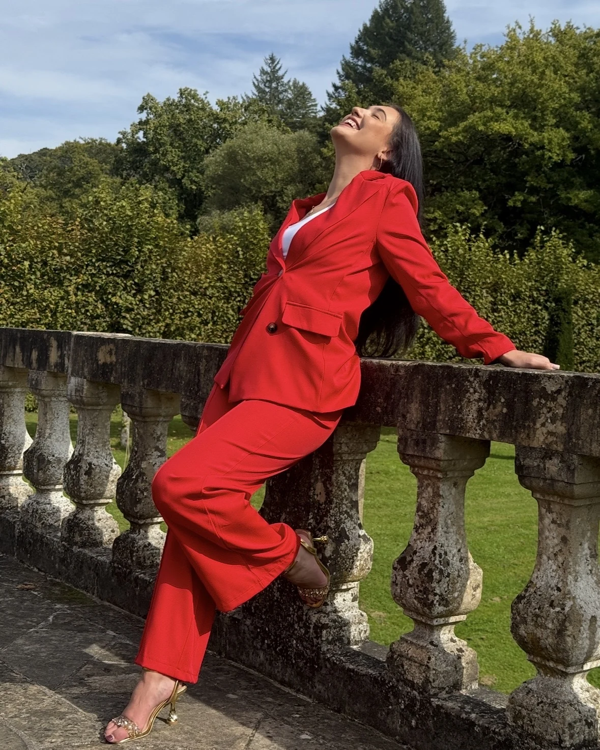 Kyra laughing in a red suit on a garden balustrade