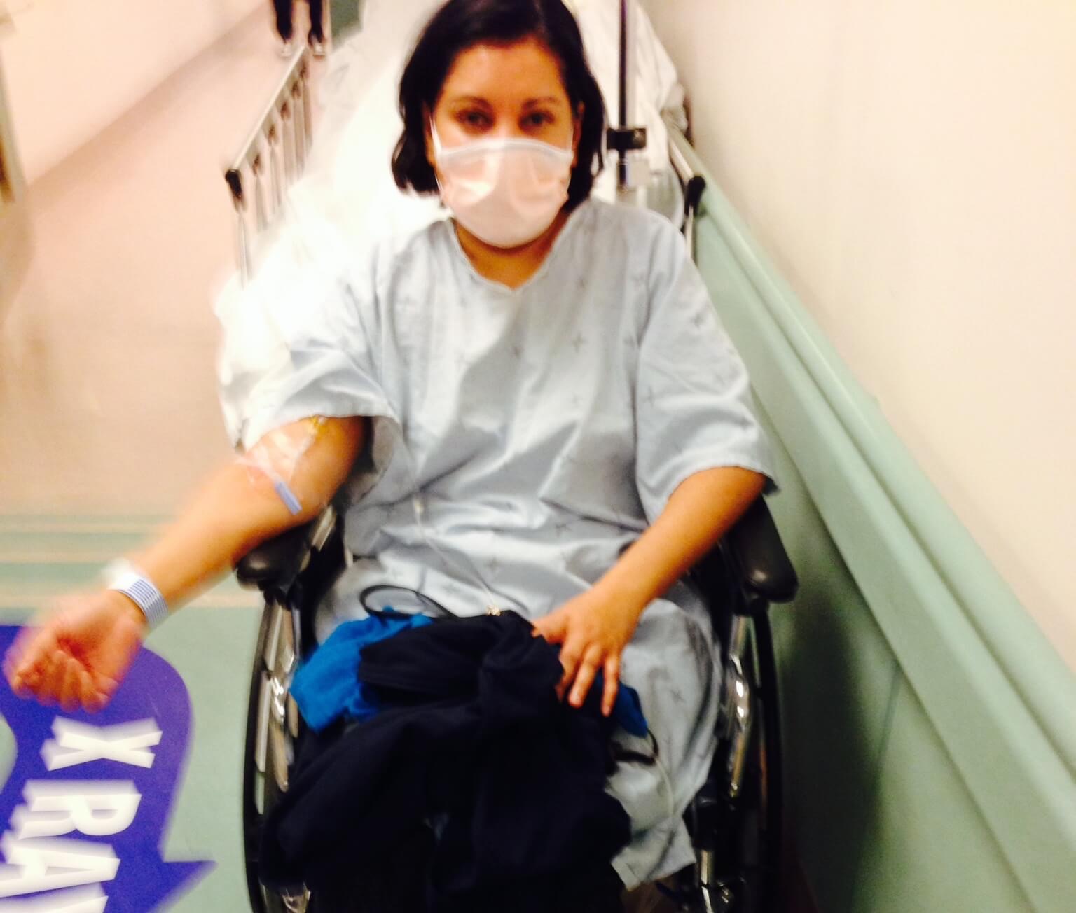 Dr. Arlini Singh in hospital gown and mask in a wheelchair during her personal health crisis — the experience that conventional medicine could not resolve and that led her to Ayurvedic medicine and founding A-YUR-VEDA Burlington Ontario