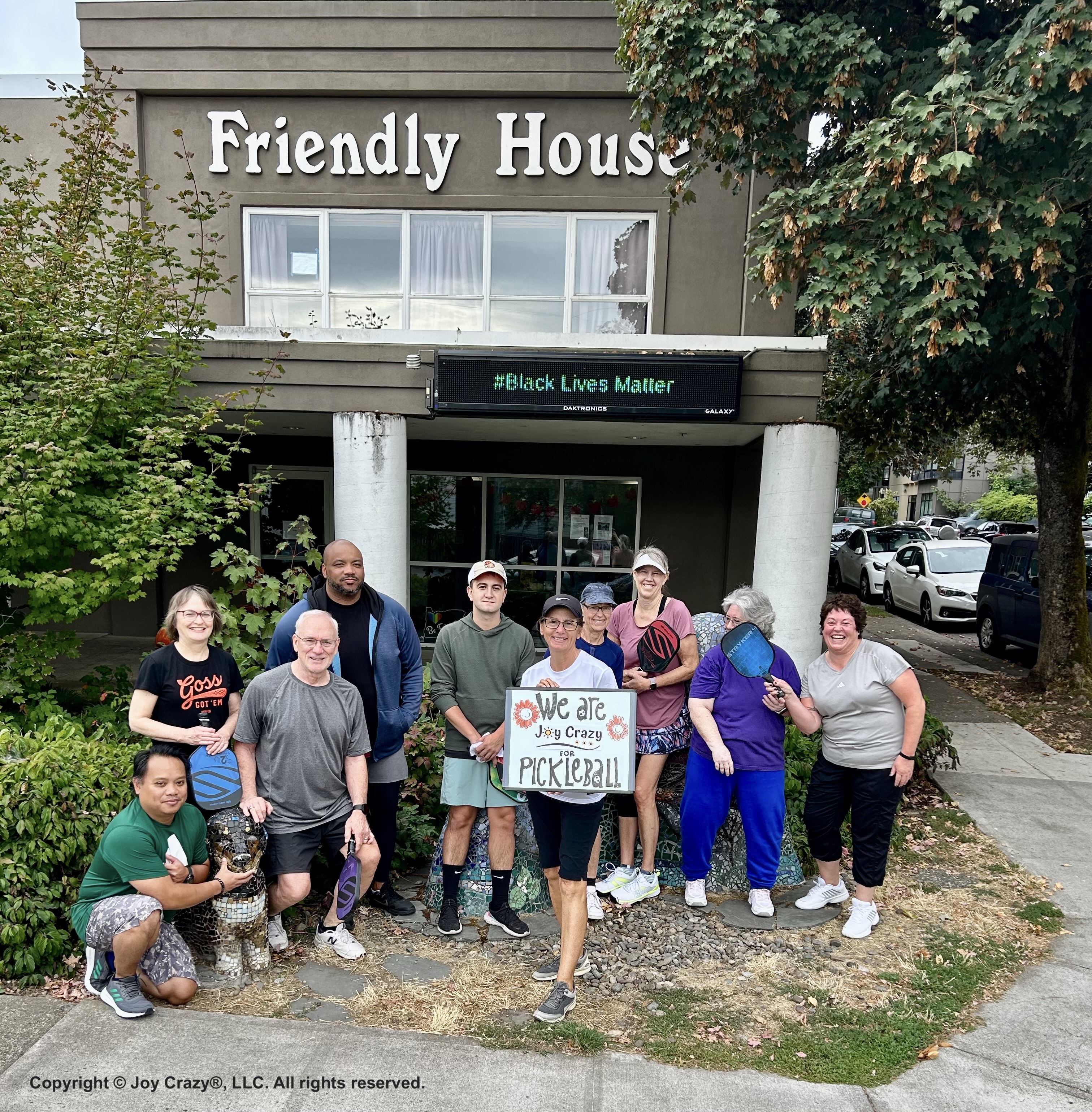 Joy Crazy® pickleball students in September, 2023 smiling in front of the Friendly House Crawford Building, pickleball paddles in hand.