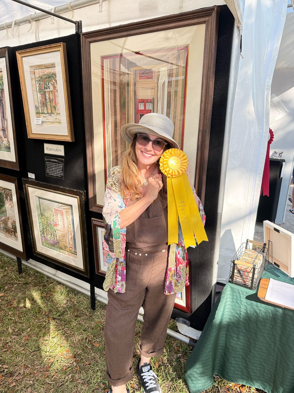 Pomm Hepner at an outdoor art show, holding a ribbon in front of her framed watercolors