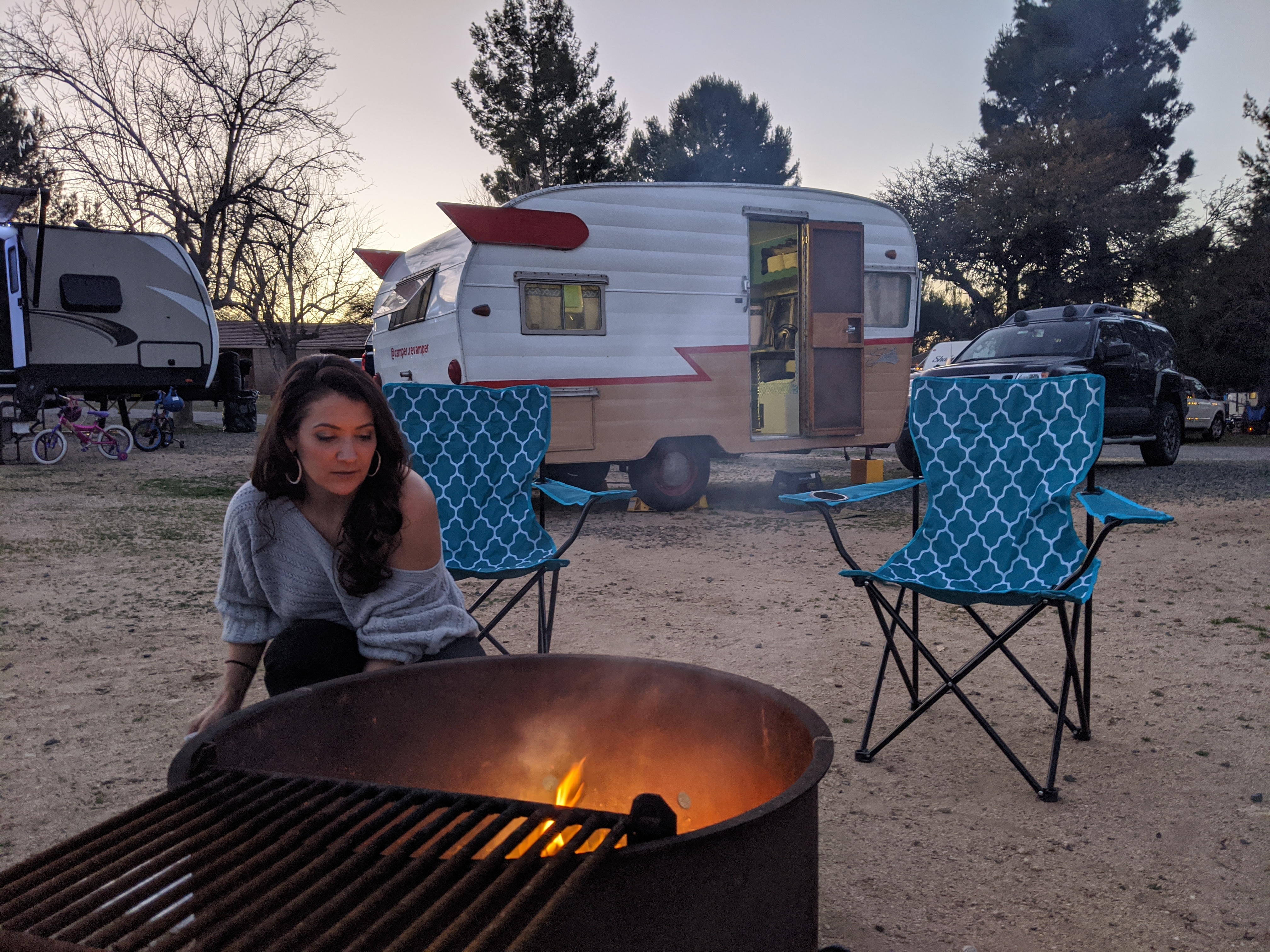 Jenna by a campfire at dusk with the finished vintage camper behind her