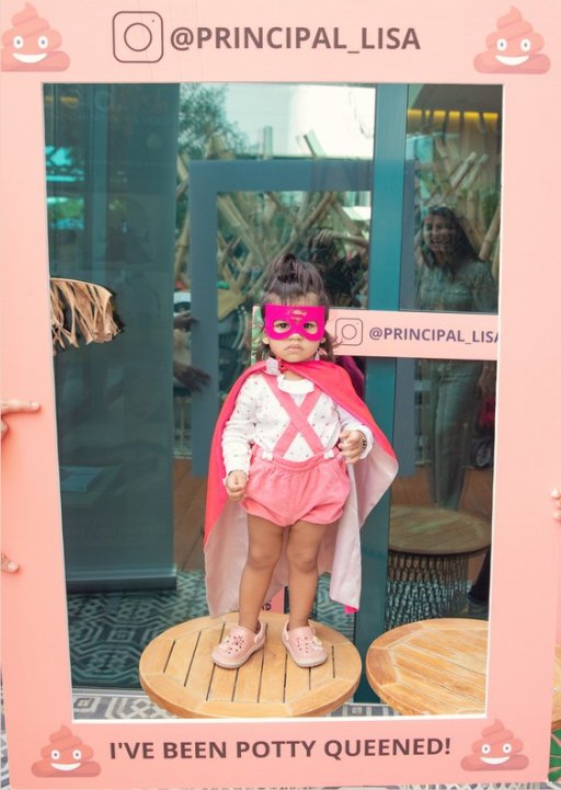 Proud toddler in a pink superhero cape inside the 'I've been Potty Queened!' photo frame
