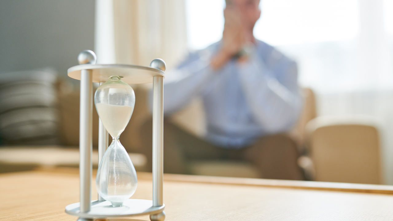 Man sitting in background with hourglass in foreground representing active surveillance and careful prostate cancer monitoring
