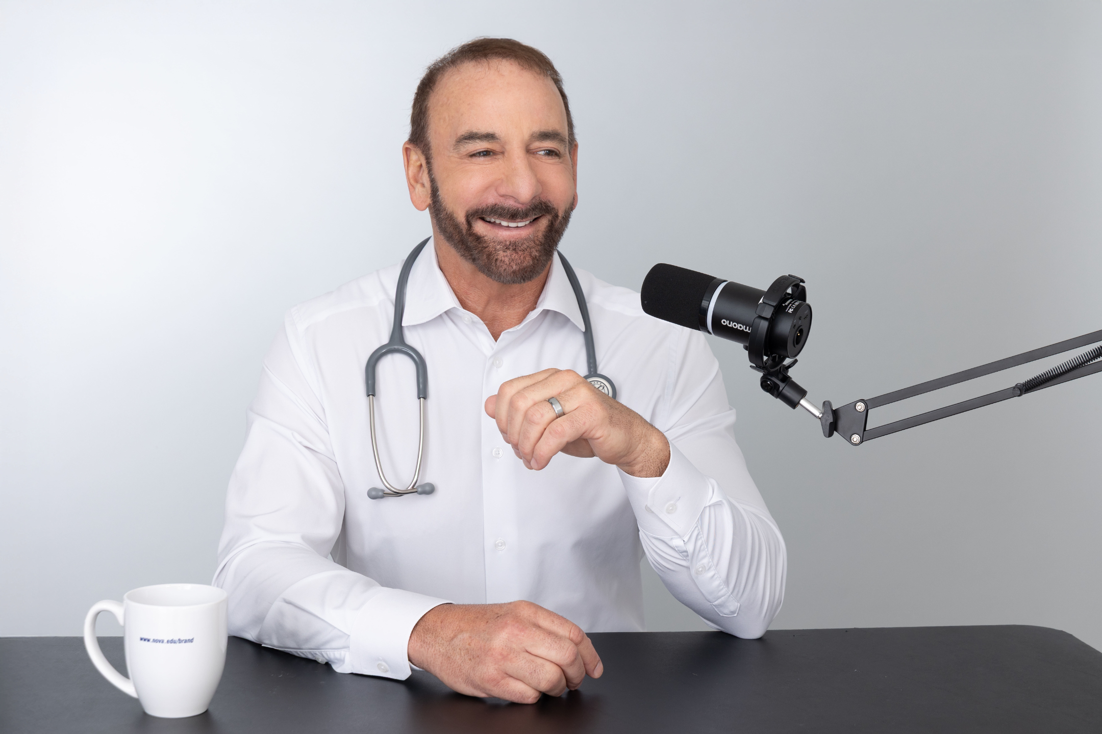 Dr. Stephen Petteruti sitting at a desk with microphone and coffee mug next to him