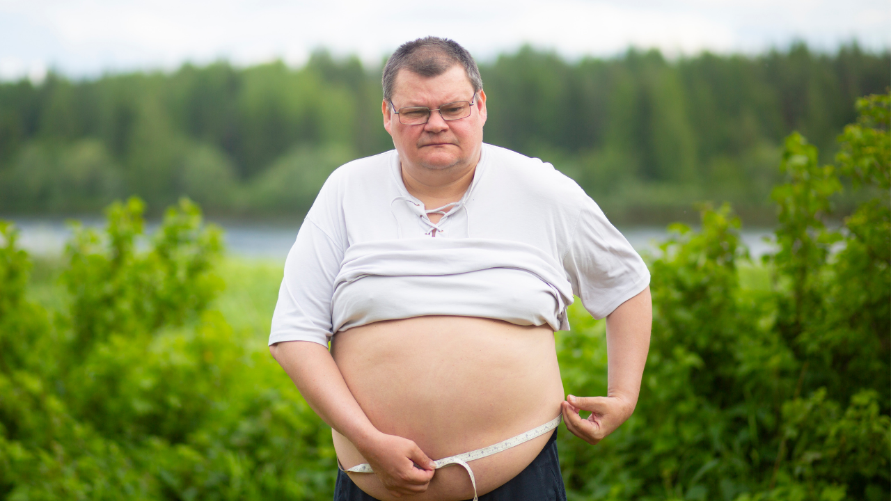 Overweight man holding a tape measure around his abdomen