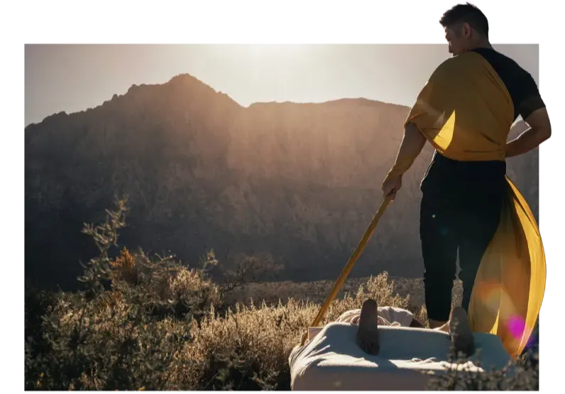 practitioner standing on a massage table with client at golden hour, facing a mountainous landscape