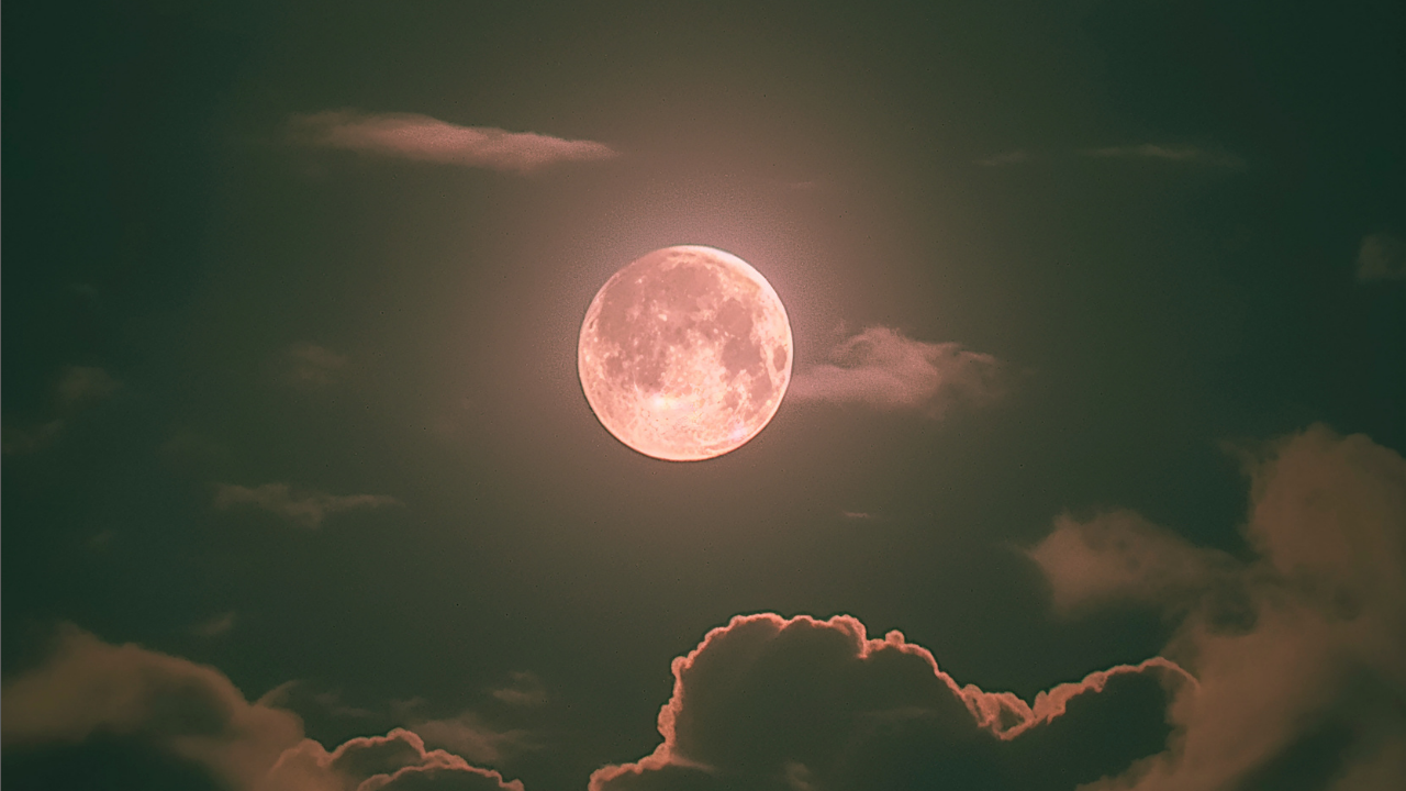 Gran luna llena con tonos cobrizos brillando en un cielo nocturno nublado, representando el eclipse lunar en Piscis y el cierre de ciclos.