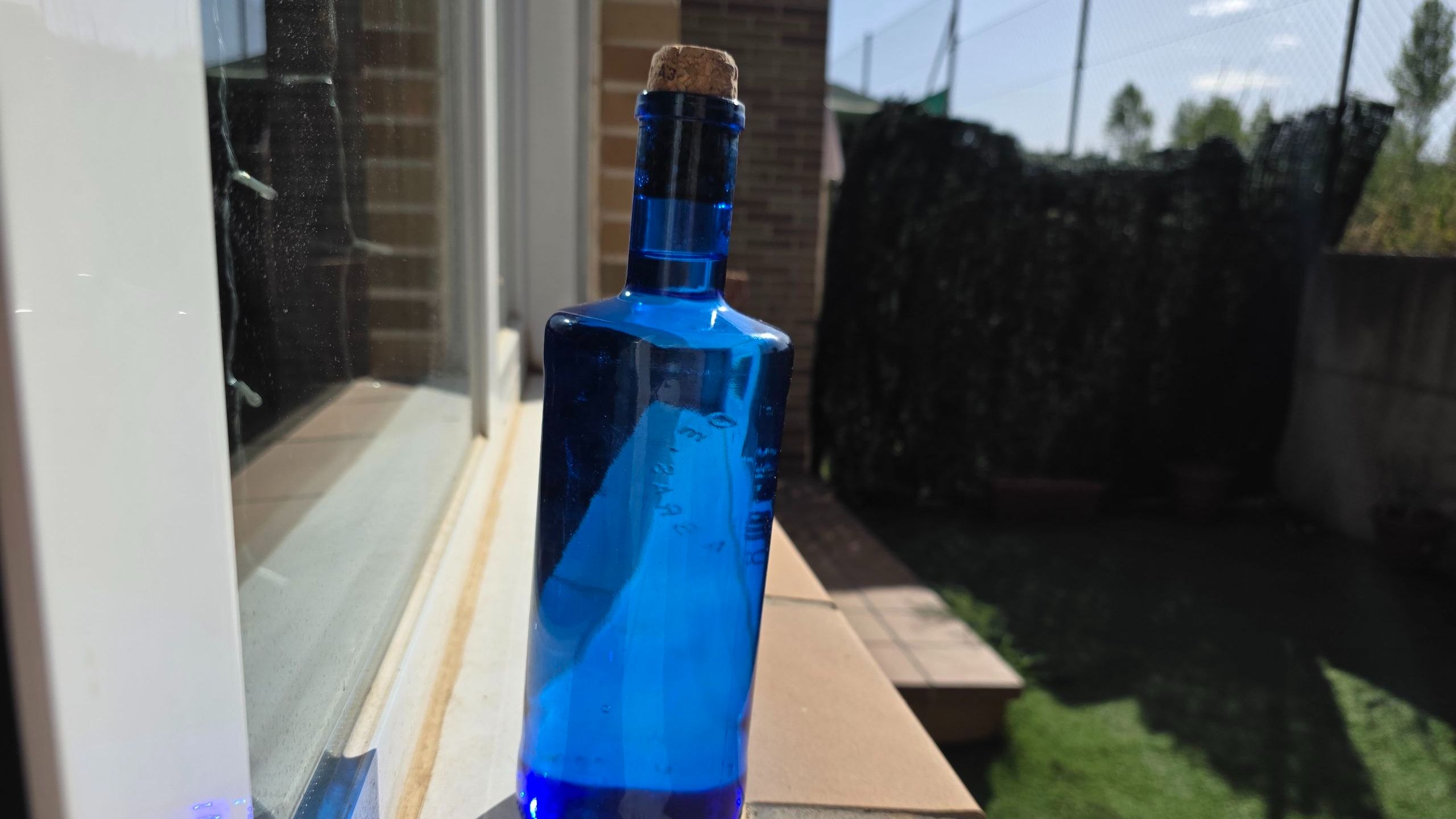 Botella de cristal azul con tapón de corcho llena de agua purificada, expuesta a la luz del sol en un alféizar para crear agua solarizada de alta vibración y limpieza energética.