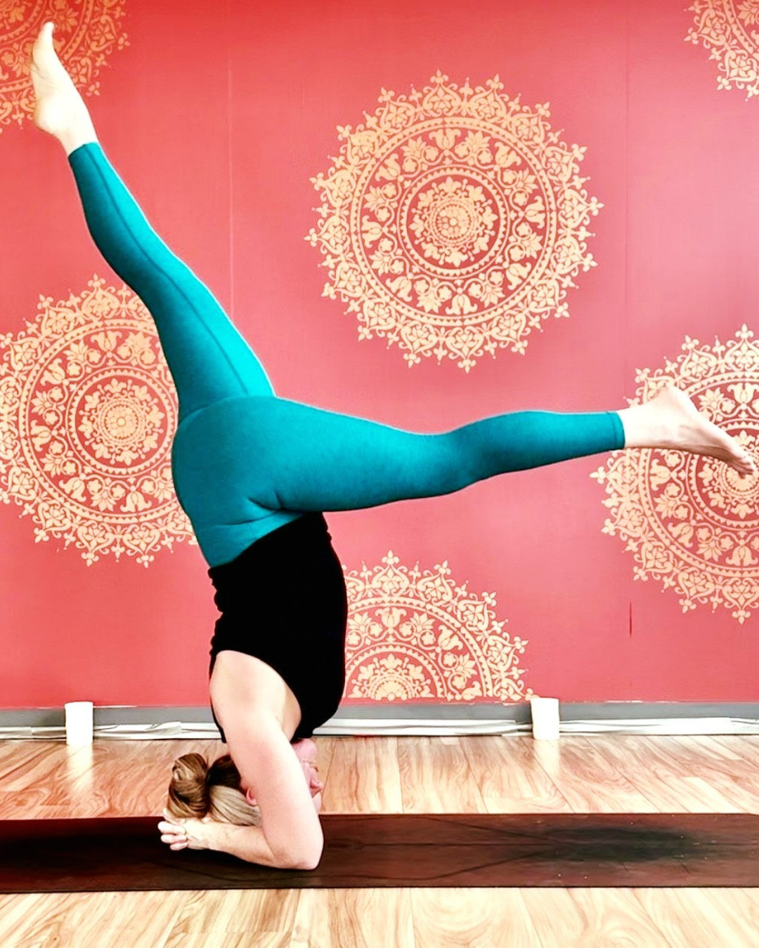A yoga teacher holding a headstand against a patterned studio wall