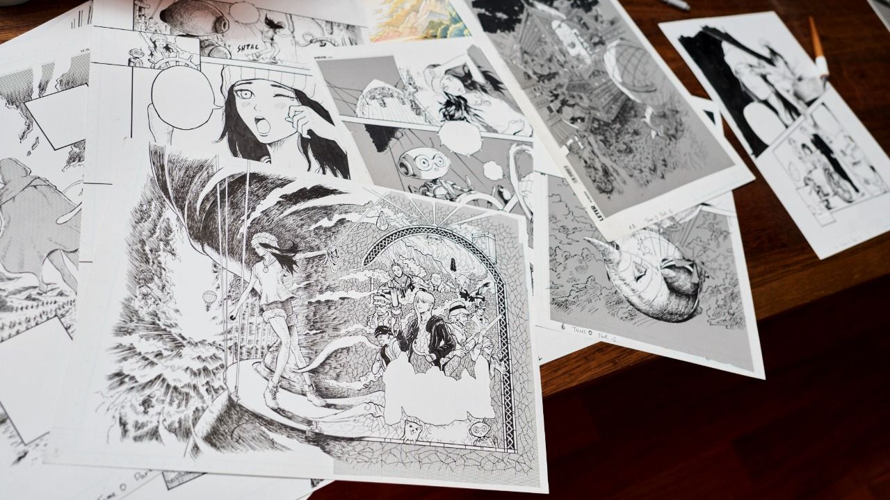 Plusieurs planches de manga terminées, encrées en noir et blanc, étalées sur une table en bois.