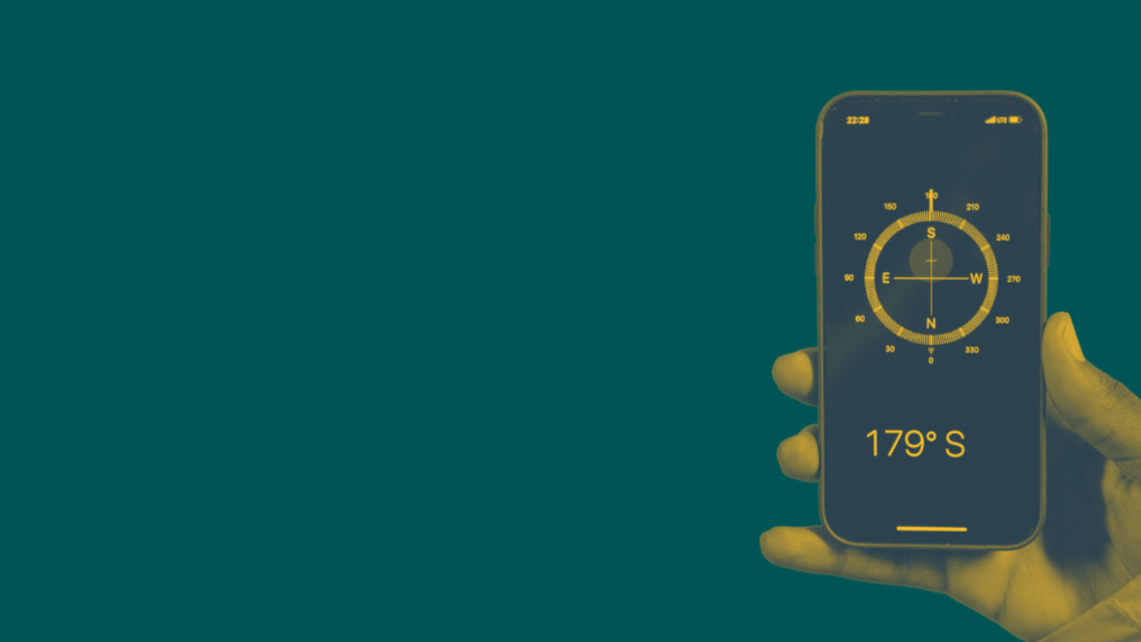 Hand holding a phone displaying a compass app, teal and yellow duotone. the post's whole argument is strategy (direction) vs. tactics (tools)