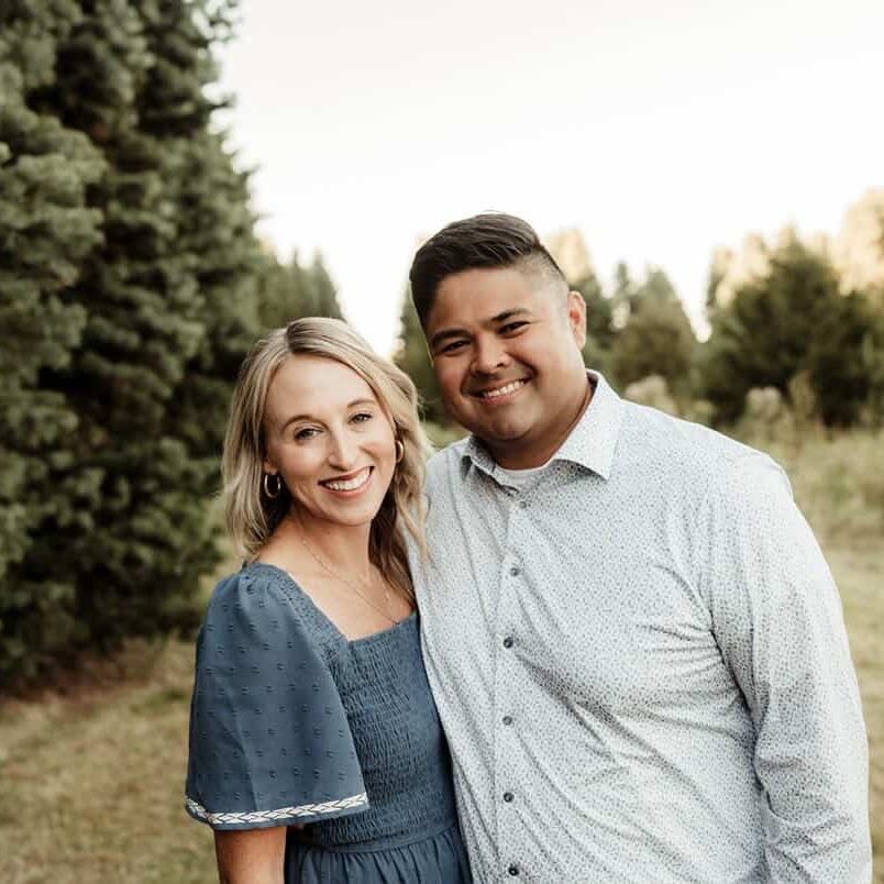 a woman and man are smiling in front of large pine trees