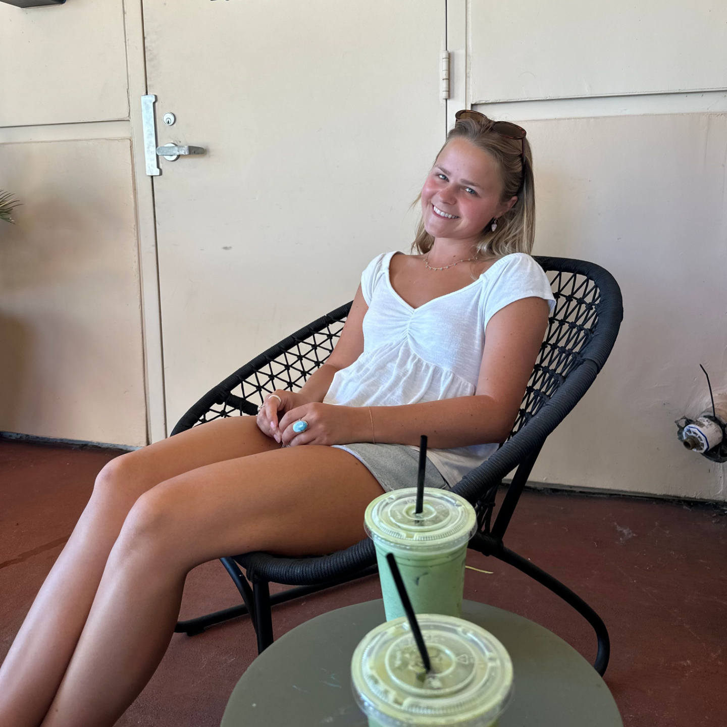 a woman sits in a chair with two coffees on the table next to her