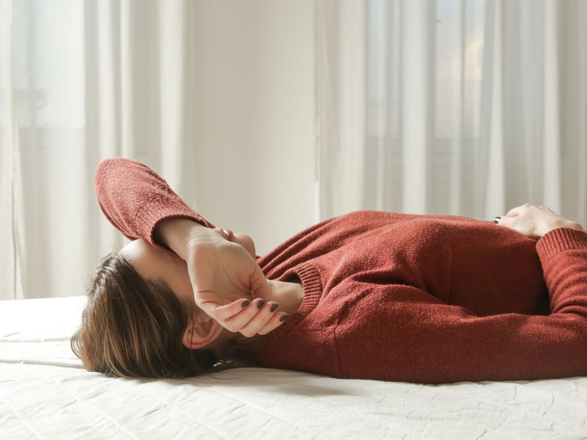 A woman in a rust jumper lying back with her arm over her eyes