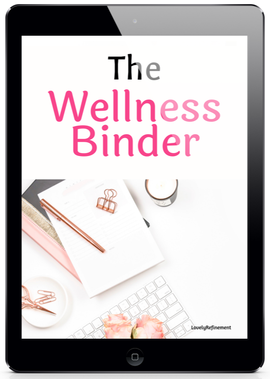 A promotional image of a black tablet displaying the cover of “The Wellness Binder” by Lovely Refinement. The cover features large black and pink text on a clean white background. Below the title is a soft, feminine desk flat lay with an open notebook, rose gold pen, binder clip, paper clips, keyboard, candle, pink flowers, and light stationery accents. The overall design feels organized, calming, polished, and wellness-focused.